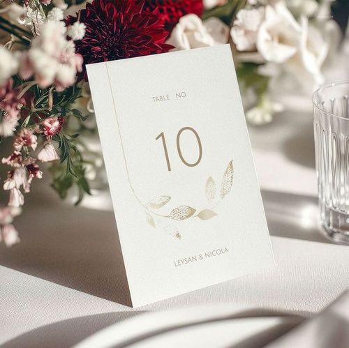 Elegant floral wedding menu card mockup featuring gold accents and table number, surrounded by glassware and blooms.