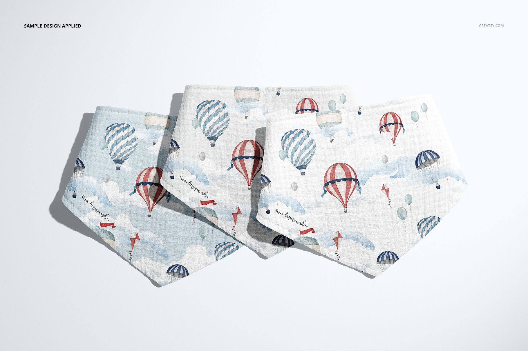 PSD mockup showing three baby muslin bandanas with a soft, textured fabric and playful balloon designs.