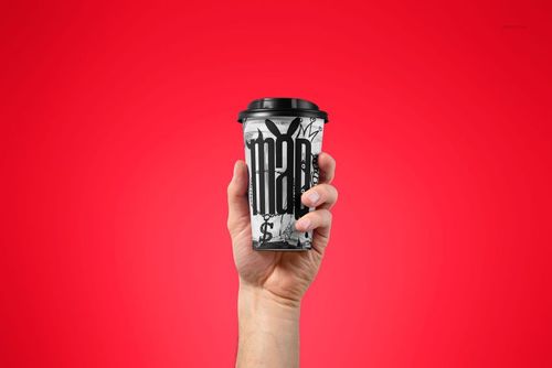 Close-up of a paper coffee cup mockup with black lid, held in a hand against a vibrant red backdrop.