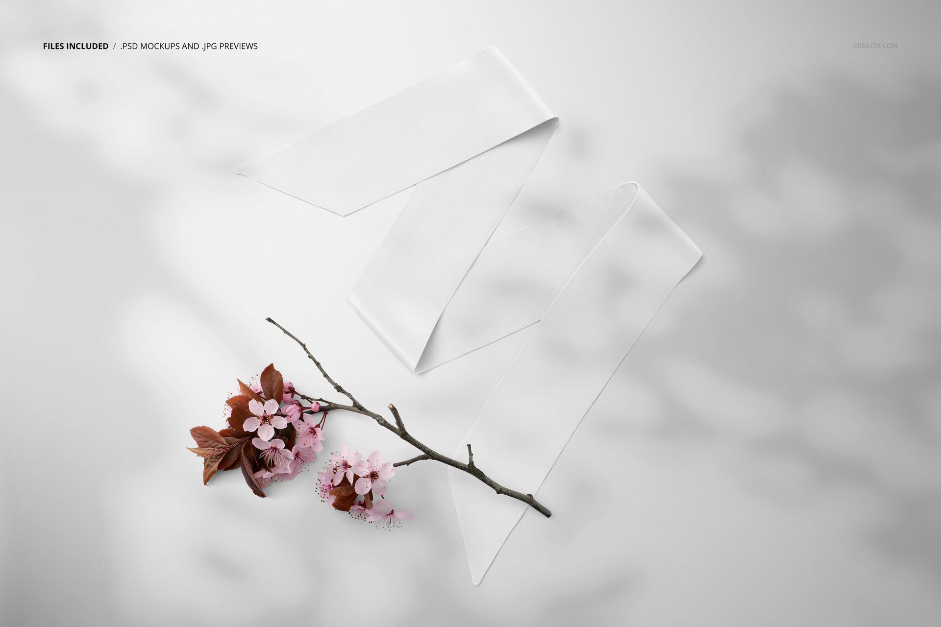 Top view of a white twilly scarf mockup placed beside a branch with pink flowers and brown leaves on a light surface.
