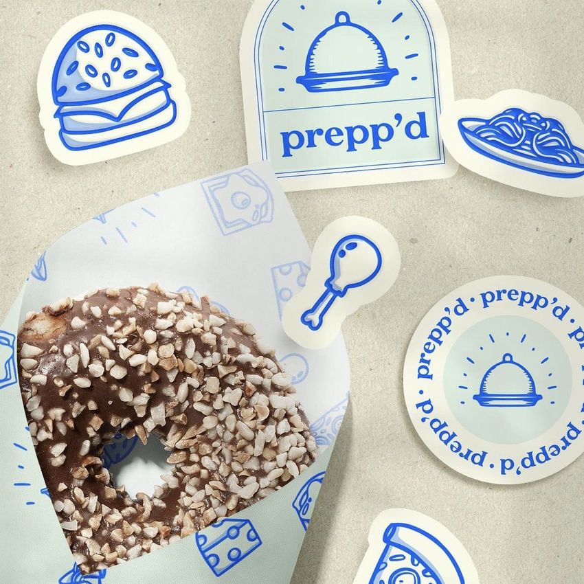 Food safe paper mockup featuring a chocolate donut with chopped nuts, wrapped in patterned paper, surrounded by blue food-themed stickers.