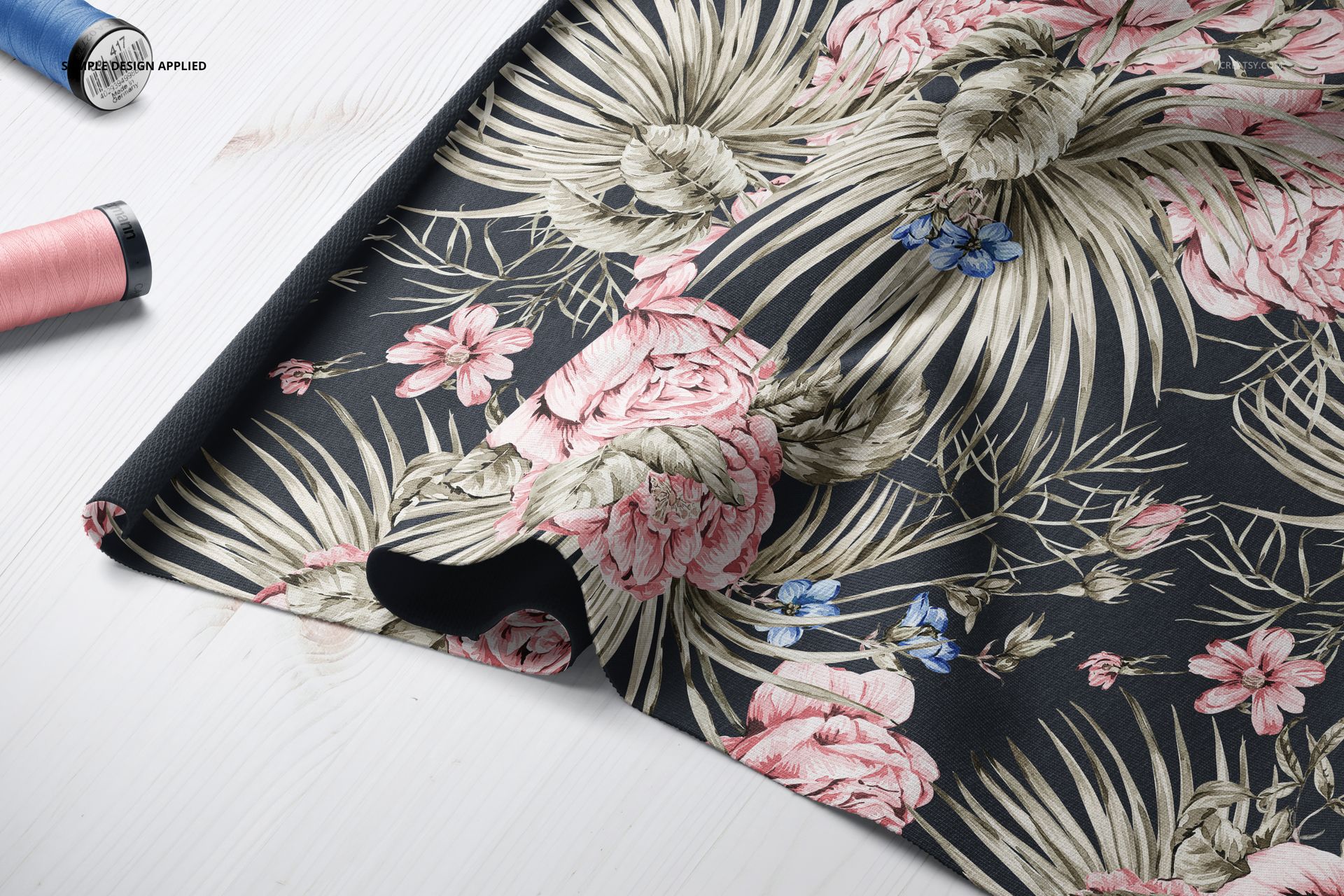 Jersey fabric mockup draped on a white wooden surface, featuring a tropical floral pattern in pink, beige, and blue.