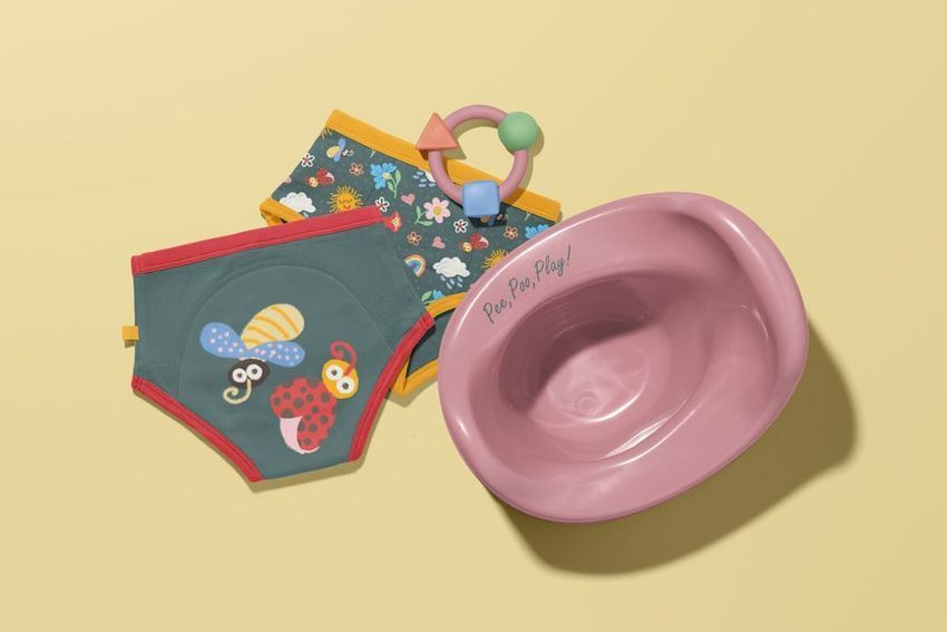 Toddler training pants mockup with playful insect illustrations, floral patterned pants, pink potty, and toy on beige background.