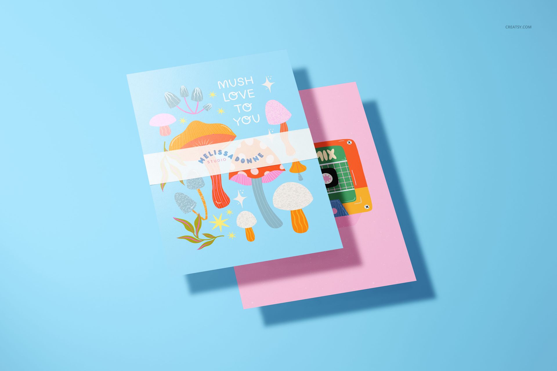A5 card mockup with playful mushroom graphics and a white ribbon, displayed with a pink envelope on a blue backdrop.