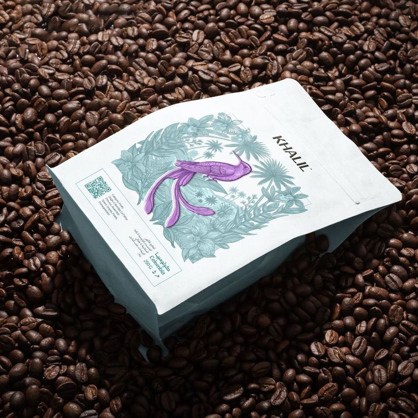 Coffee bag mockup featuring a white package with a purple fish illustration, placed on a surface covered with coffee beans.