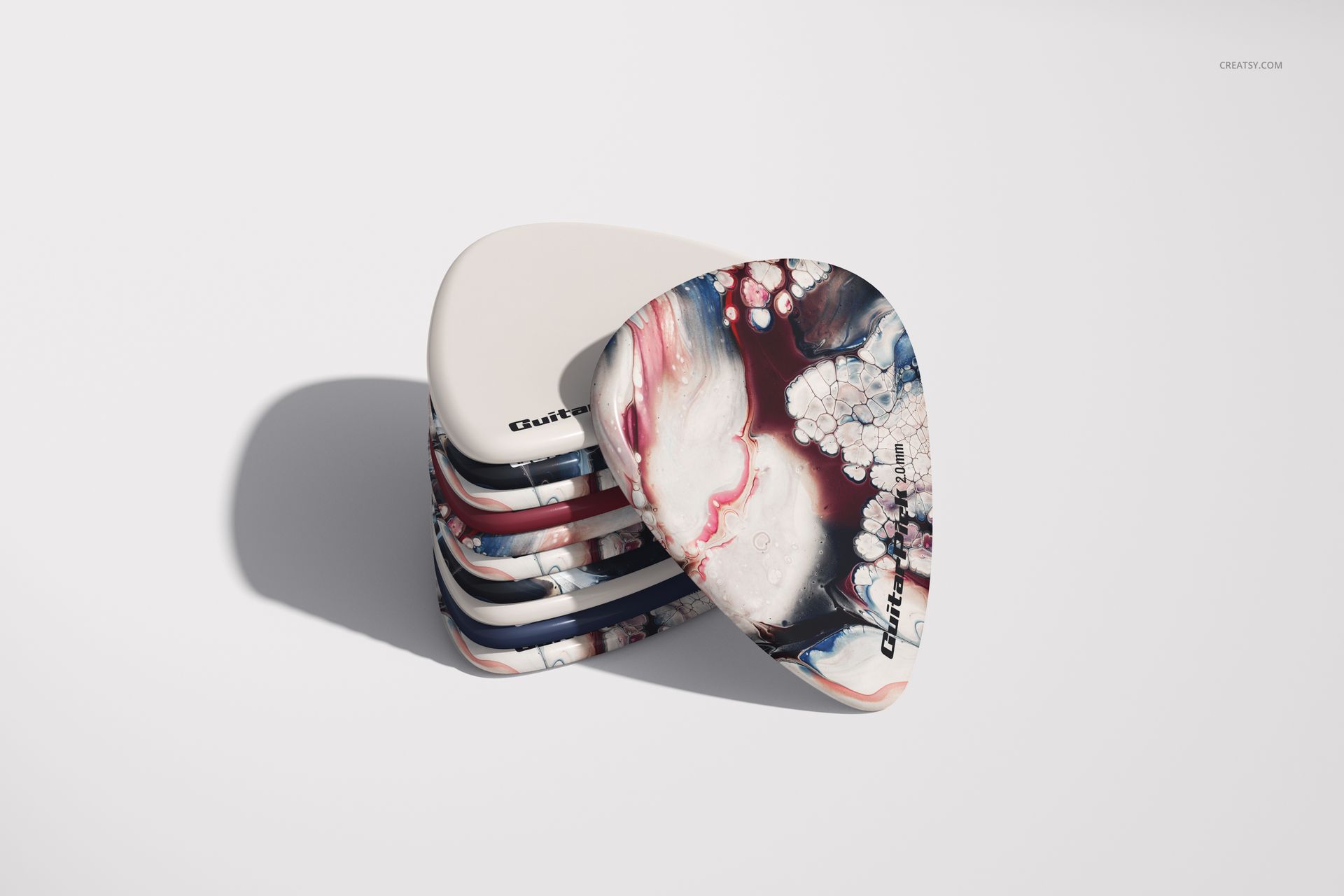 PSD mockup of guitar picks arranged in a pile, displaying a mix of plain and abstract designs with soft shadows on a light surface.
