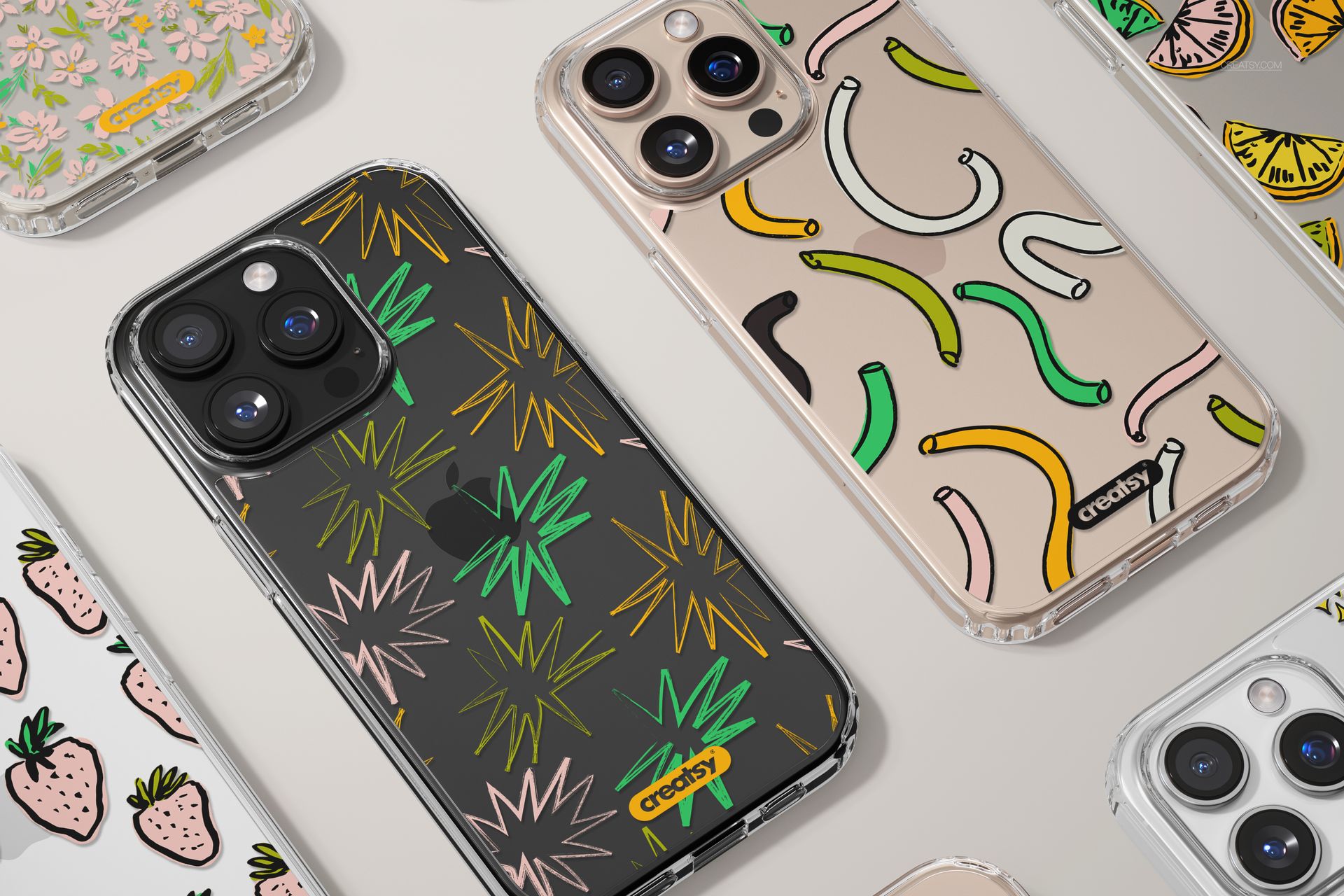 PSD mockup of multiple iPhone 16 Pro Max clear cases with playful designs, viewed from above on a light surface.