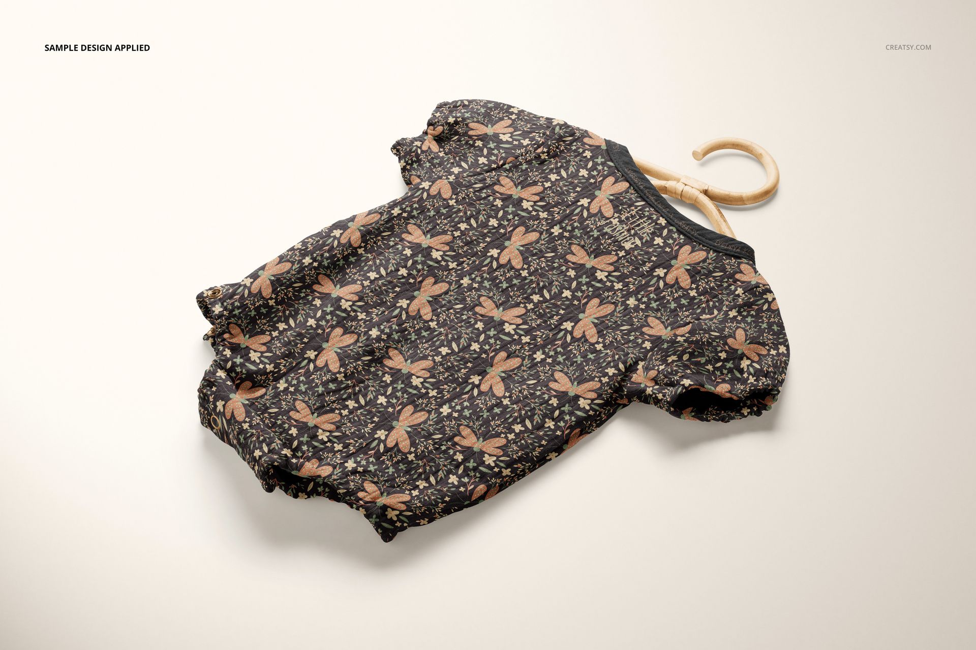 Front view of a muslin onesie mockup with short sleeves, featuring a brown dragonfly and floral pattern on a light surface.
