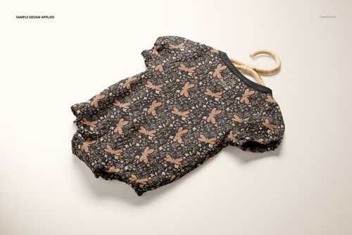 Front view of a muslin onesie mockup with short sleeves, featuring a brown dragonfly and floral pattern on a light surface.
