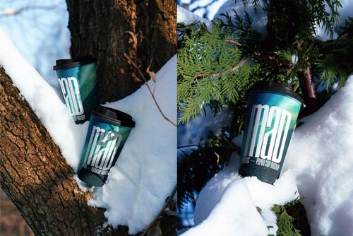 PSD mockup of drinkware featuring teal paper cups with straws and black lids placed on snow in a forest setting.