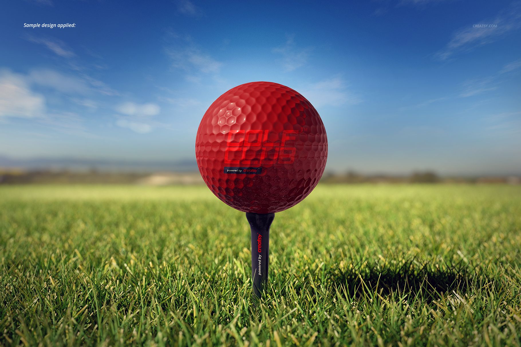 Golf ball mockup featuring a vibrant red ball on a tee, photographed outdoors on green grass with blue sky.