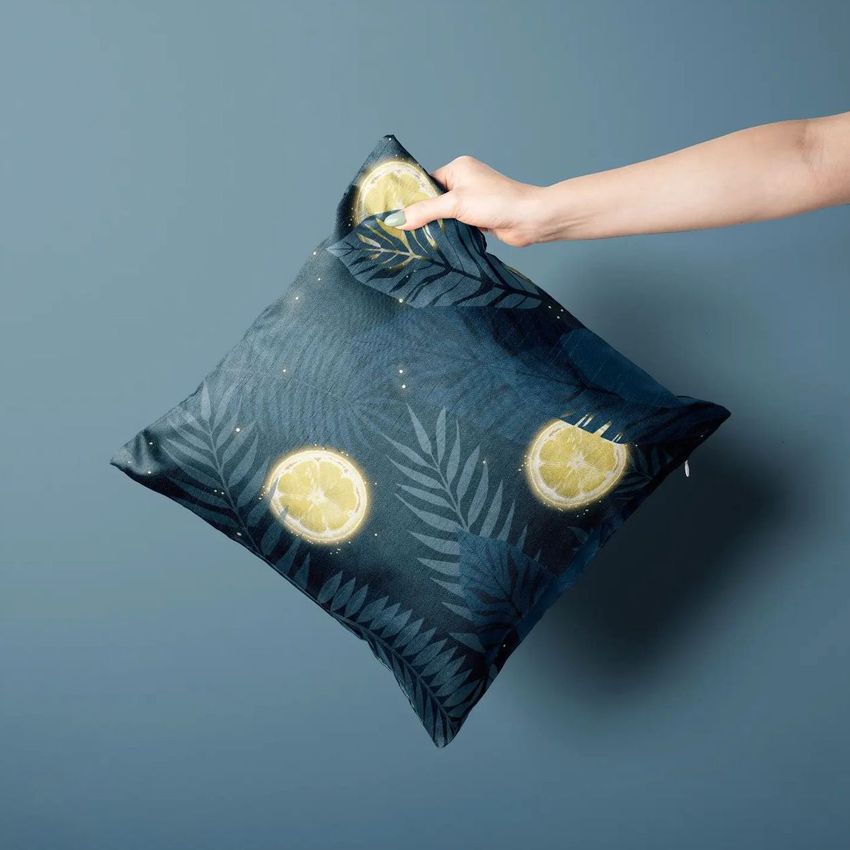 Polyester cushion cover mockup featuring a hand holding a square pillow with a dark blue background and tropical leaf and lemon patterns.