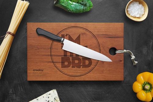 Top view of a rectangular engraved wooden board mockup with a chef's knife, surrounded by vegetables and cheese.