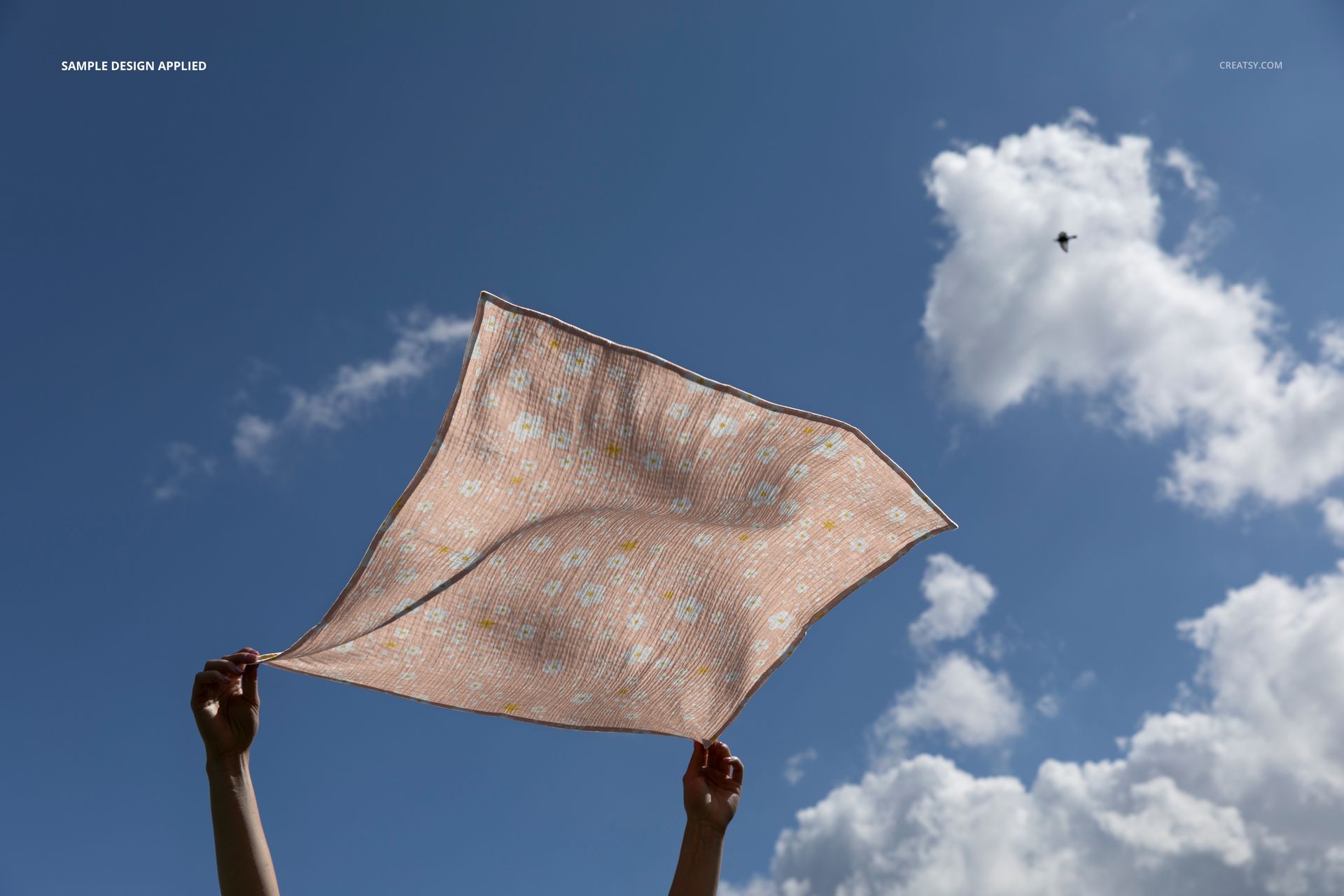 Crinkle muslin swaddle blanket mockup featuring a pastel floral design, held up to a bright sky with clouds.