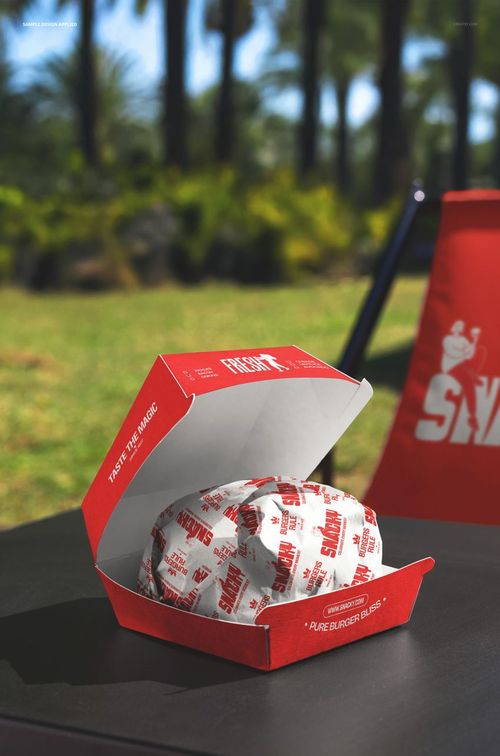 Front view of a red burger box mockup with a wrapped burger inside, placed on a black surface outdoors.
