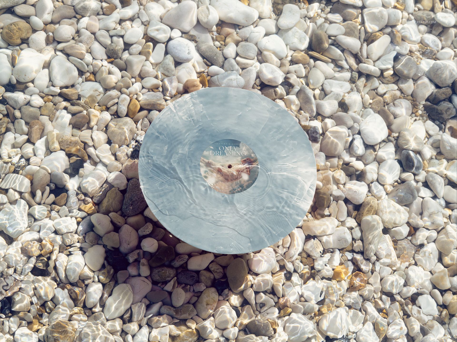 Special effects vinyl record mockup featuring a swirl pattern, resting among sunlit stones under shallow water.