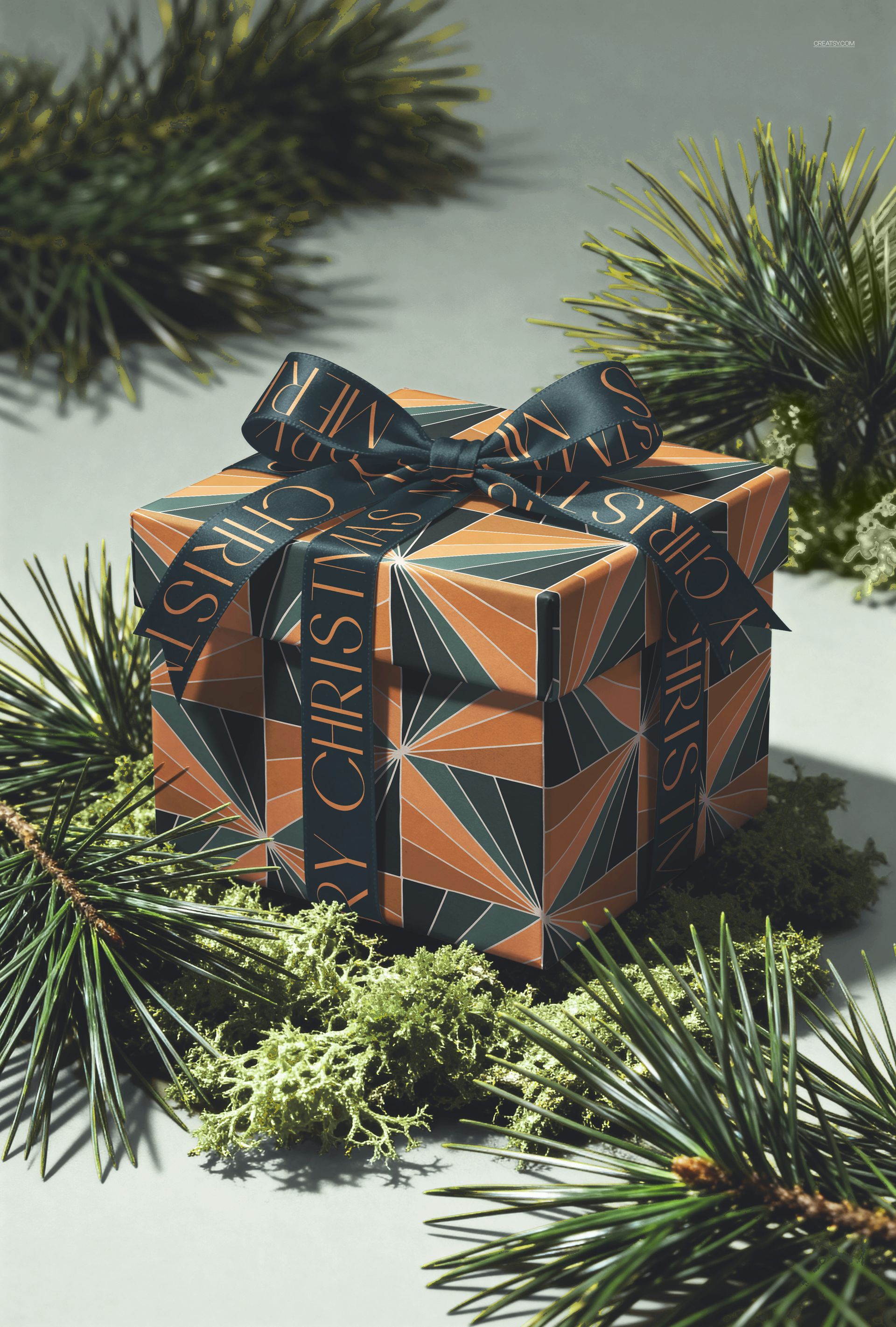 Christmas gift box mockup with geometric pattern and ribbon, surrounded by pine branches and moss, front view.