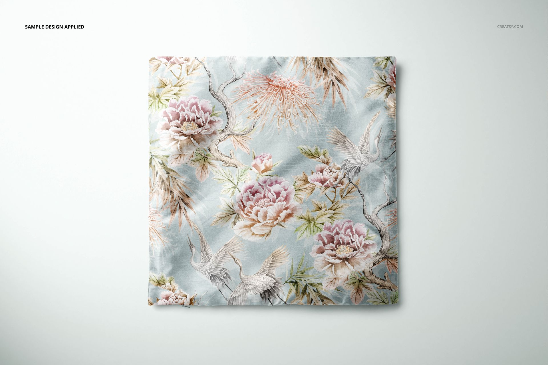 Top view of a polyester cushion cover mockup featuring pink peonies and cranes on a pale blue background.
