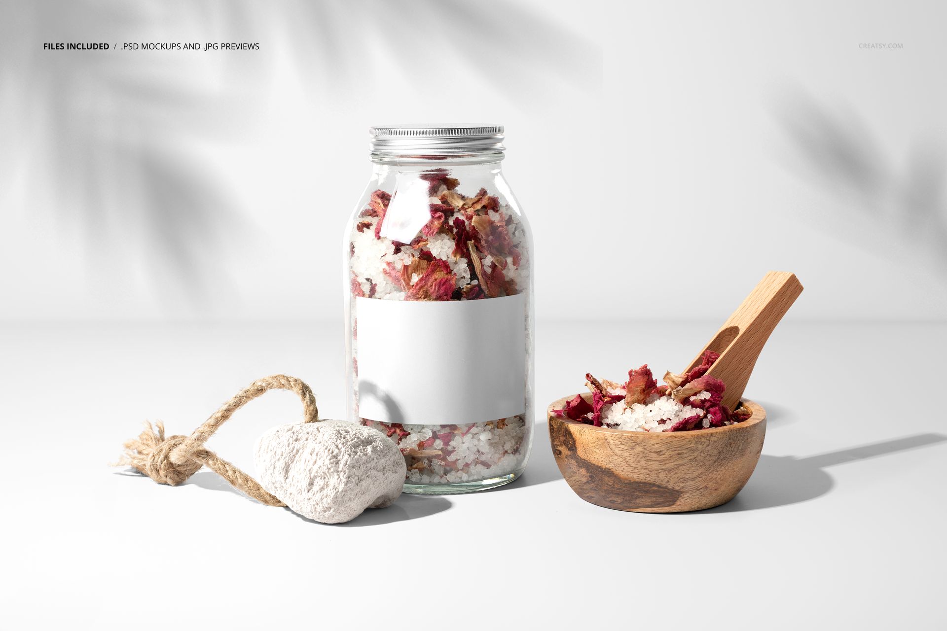 Front view of a clear glass jar filled with bath salts and rose petals, featuring a blank white label for mockup use.