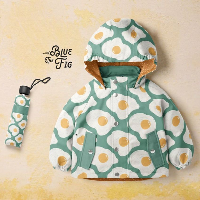 Kids rainwear mockup featuring a hooded jacket and umbrella with a playful fried egg pattern on a light yellow background.