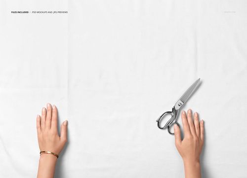 Top view of uncut cotton fabric sample mockup with two hands and a pair of metal scissors on a plain surface.