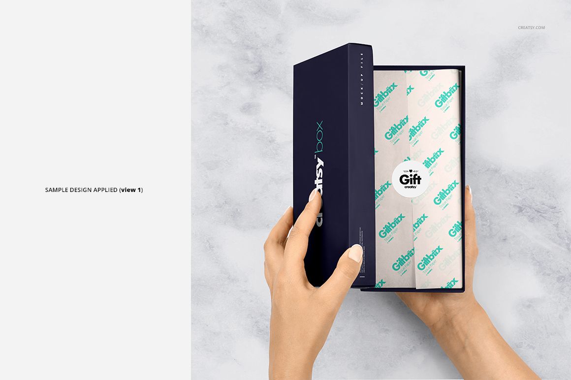 Rectangular gift box mockup with patterned tissue paper inside, held by hands over a gray marble surface, PSD mockup.