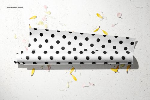 Top view of a mockup featuring white wrapping paper with black dots, surrounded by yellow and pink flower petals.