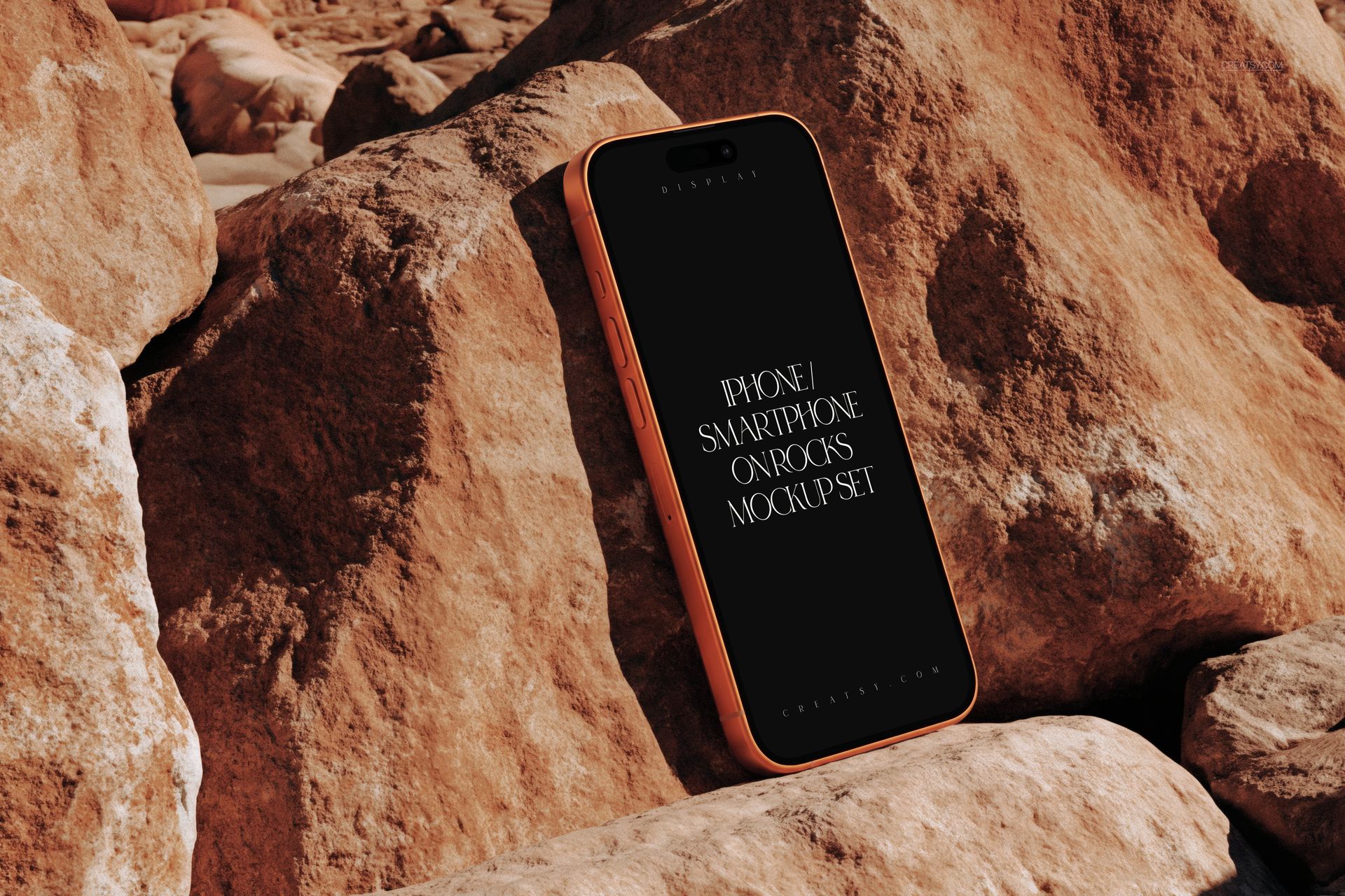 PSD mockup of an iPhone smartphone resting upright on rugged tan rocks, with a dark display and angled view.