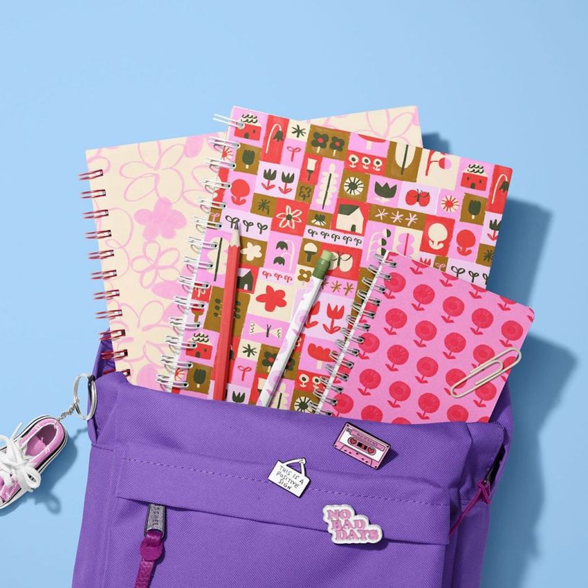 School backpack mockup with spiral notebooks in colorful floral and geometric covers, arranged on a light blue background.