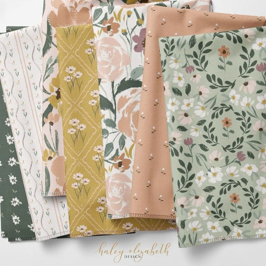 Folded fabrics mockup featuring five pieces with floral and geometric patterns in green, peach, cream, and pink tones on a light surface.