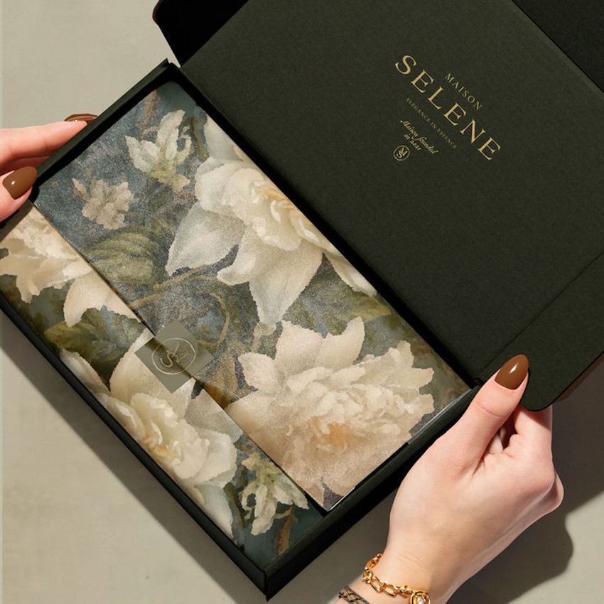Hands holding an open mailing box mockup with floral-patterned tissue paper and gold text on the inner lid.