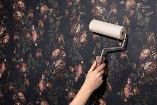 Non-woven vinyl wallpaper mockup showing a hand rolling out wallpaper with a rich floral pattern on a wall.