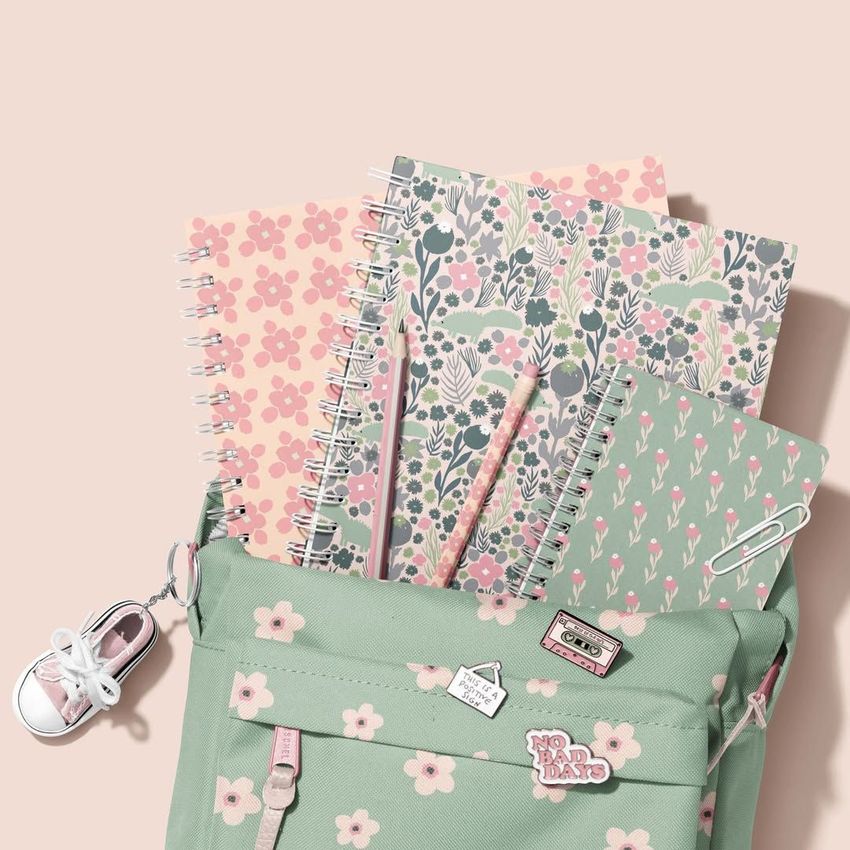 School backpack mockup in pastel green with floral pattern, filled with spiral notebooks featuring botanical and floral covers.