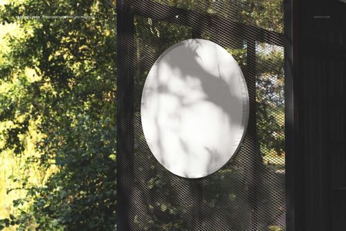 Round outdoor signboard mockup featuring a blank white circular sign mounted on a mesh panel with greenery in the background.