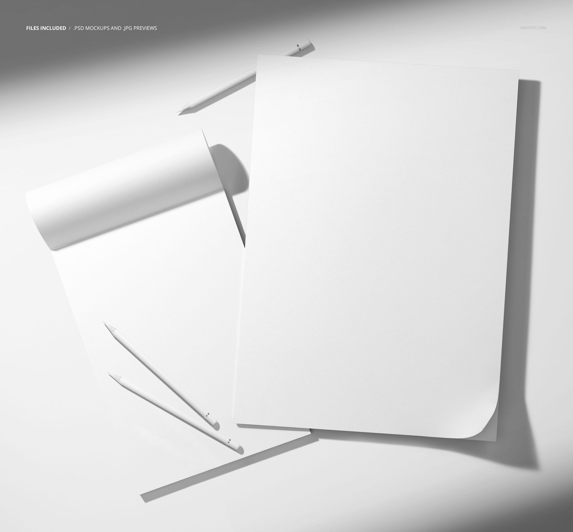 PSD mockup featuring two empty paper pads and three pencils arranged on a neutral background under soft lighting.
