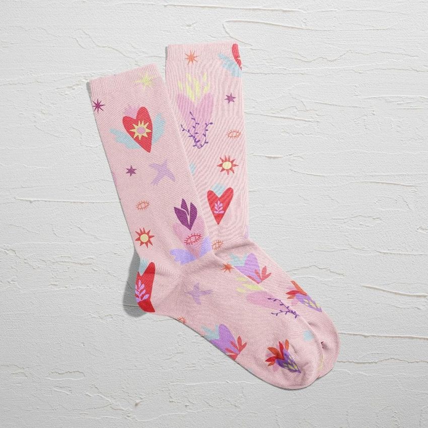 Socks mockup featuring a pair of light pink socks with colorful heart, flower, and abstract patterns on a textured white surface.