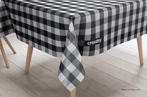Black and white plaid tablecloth mockup displayed on a light wood table with angled legs in a kitchen scene.