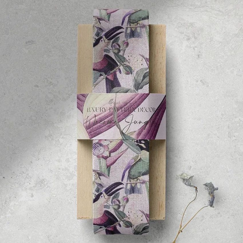 Wide cotton ribbon mockup featuring a botanical pattern in muted purple and green tones, wrapped around a wooden block on a light textured surface.