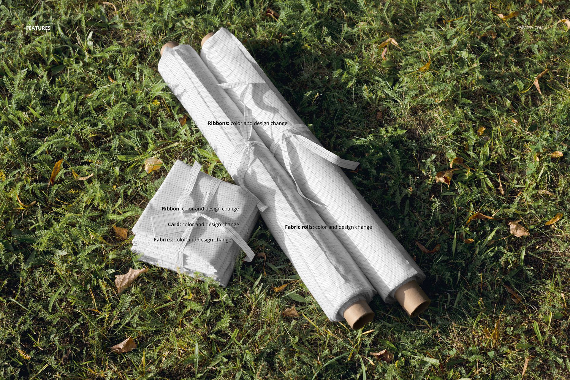 PSD mockup showing two rolled fabrics and a folded fabric stack with grid pattern on a natural grass meadow.