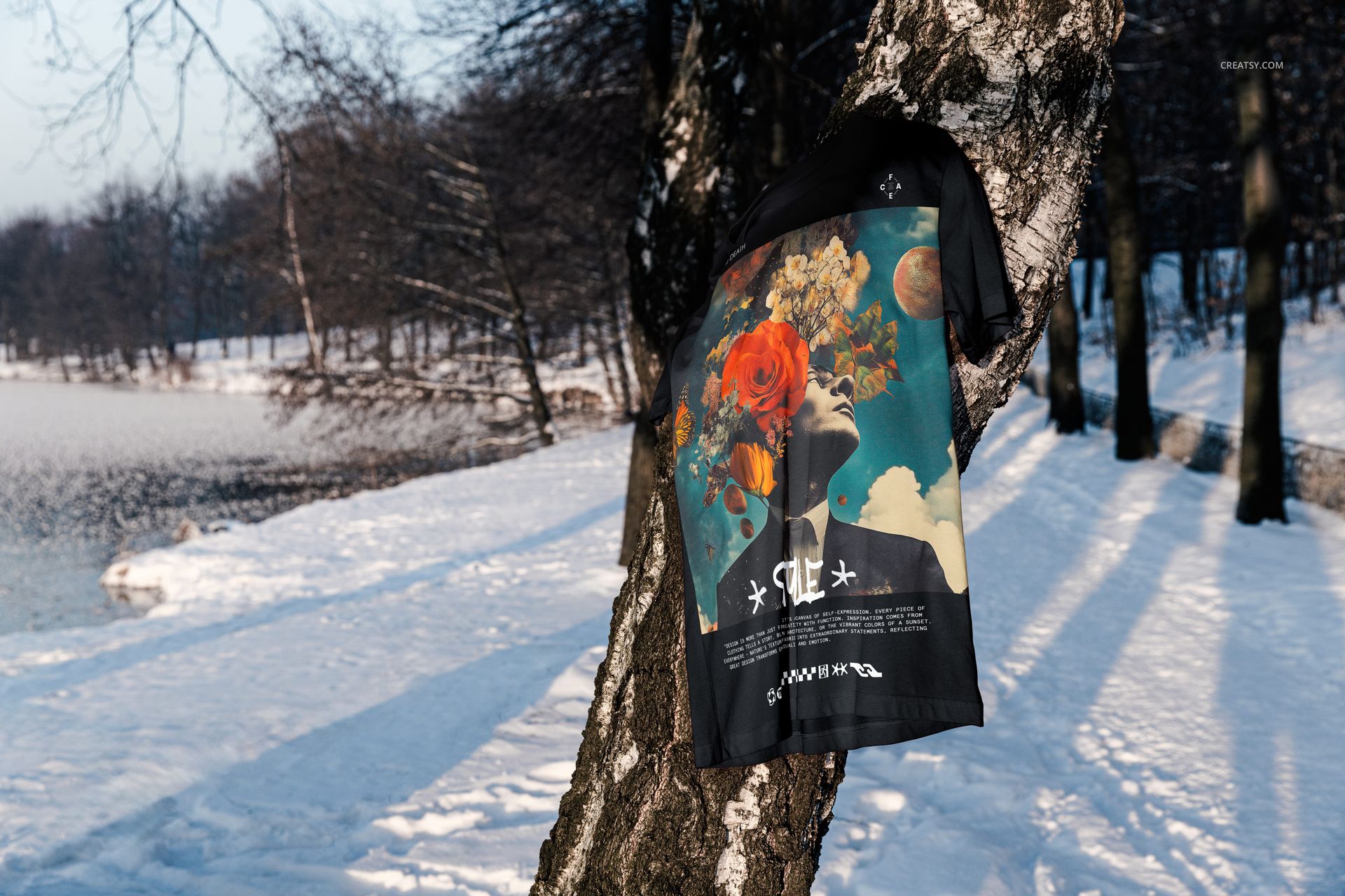 Bella Canvas 3001 t-shirt mockup featuring a bold design, displayed on a tree with snow and a frozen lake in the background.