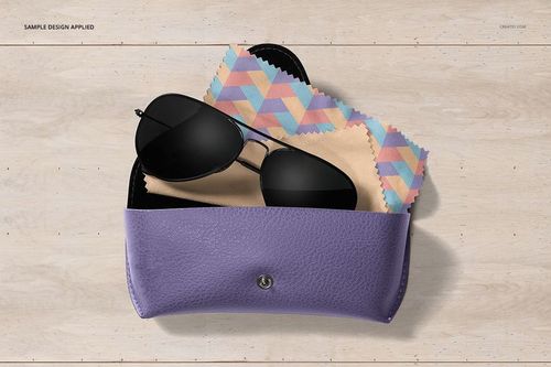 Top view of a mockup set featuring a patterned microfiber cleaning cloth, sunglasses, and a purple case on wood.