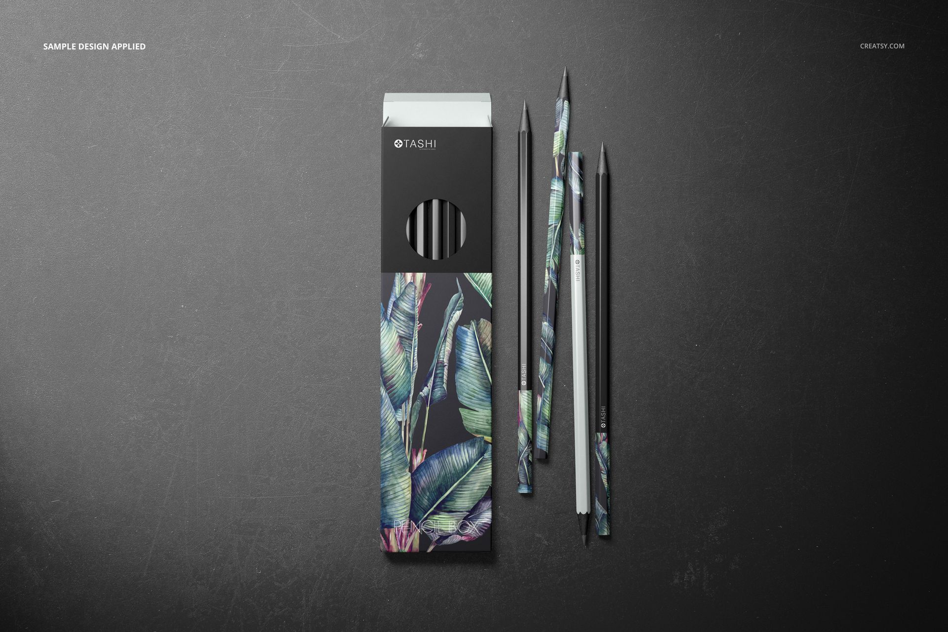 Pencil box mockup set featuring a black box and pencils with botanical leaf designs, arranged on a dark background.
