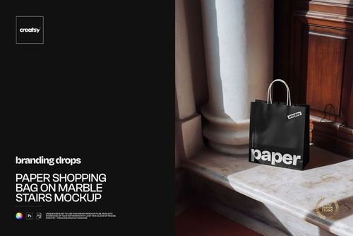 Paper shopping bag mockup featuring a black bag with bold white text, positioned on marble steps in natural light.