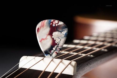 Detailed PSD mockup showing a single artistic guitar pick placed across guitar strings, highlighting its vibrant colors and texture.