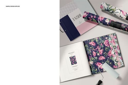 Wallpaper sample book mockup with open pages showing floral patterns, rolled wallpaper, and a paint roller on a light surface.