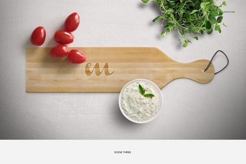 Top view of a wooden chopping board mockup with tomatoes, tzatziki dip, and fresh herbs on a white background.
