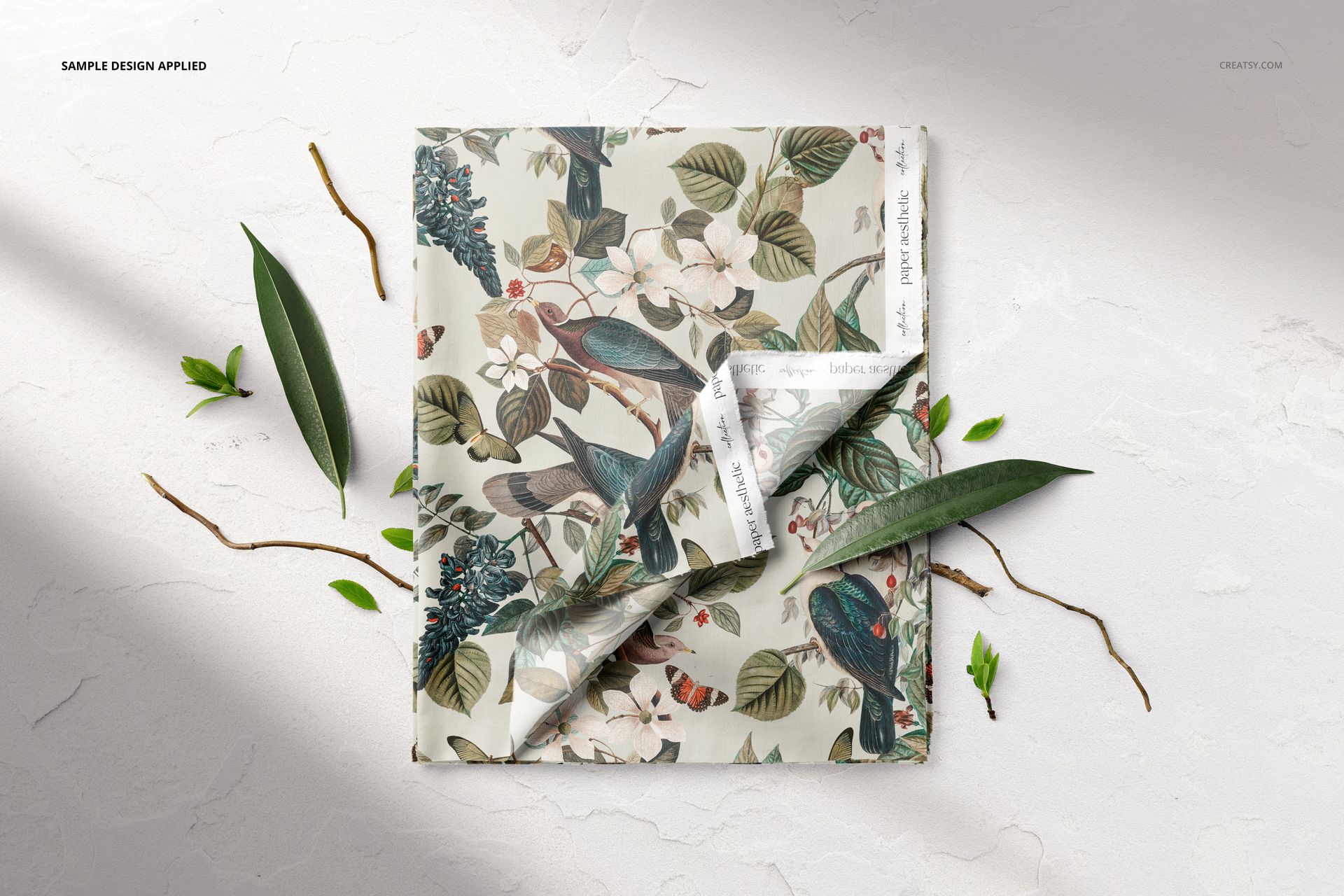 Botanical-themed folded fabric mockup featuring birds and flowers, shown on a white background with natural props.