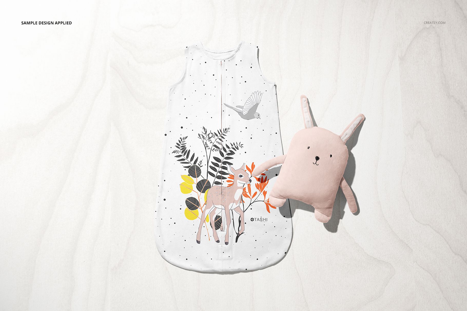 Baby wearable blanket mockup featuring animal and plant illustrations, displayed with a pink bunny plush on a neutral background.