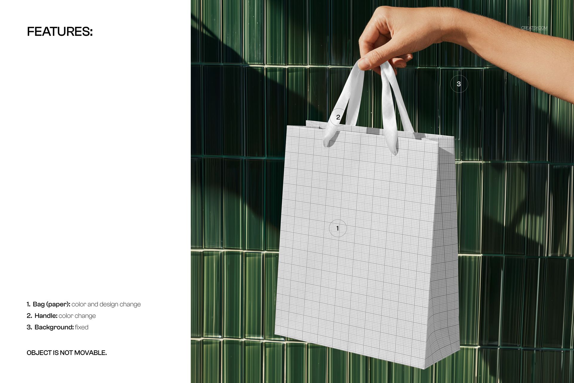 Close-up of a person’s hand holding a mockup shopping bag with a grid design and white handles in front of green tiles.