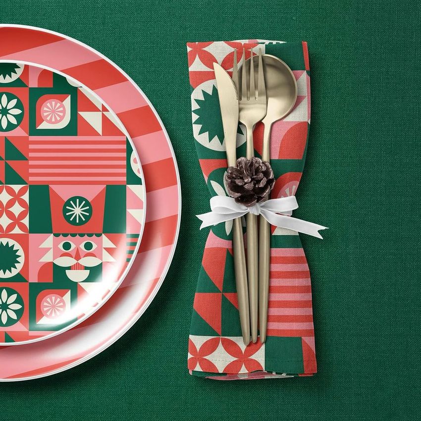 Christmas-themed plate, napkin, and tablecloth mockup featuring geometric nutcracker and snowflake patterns in red, green, and white.